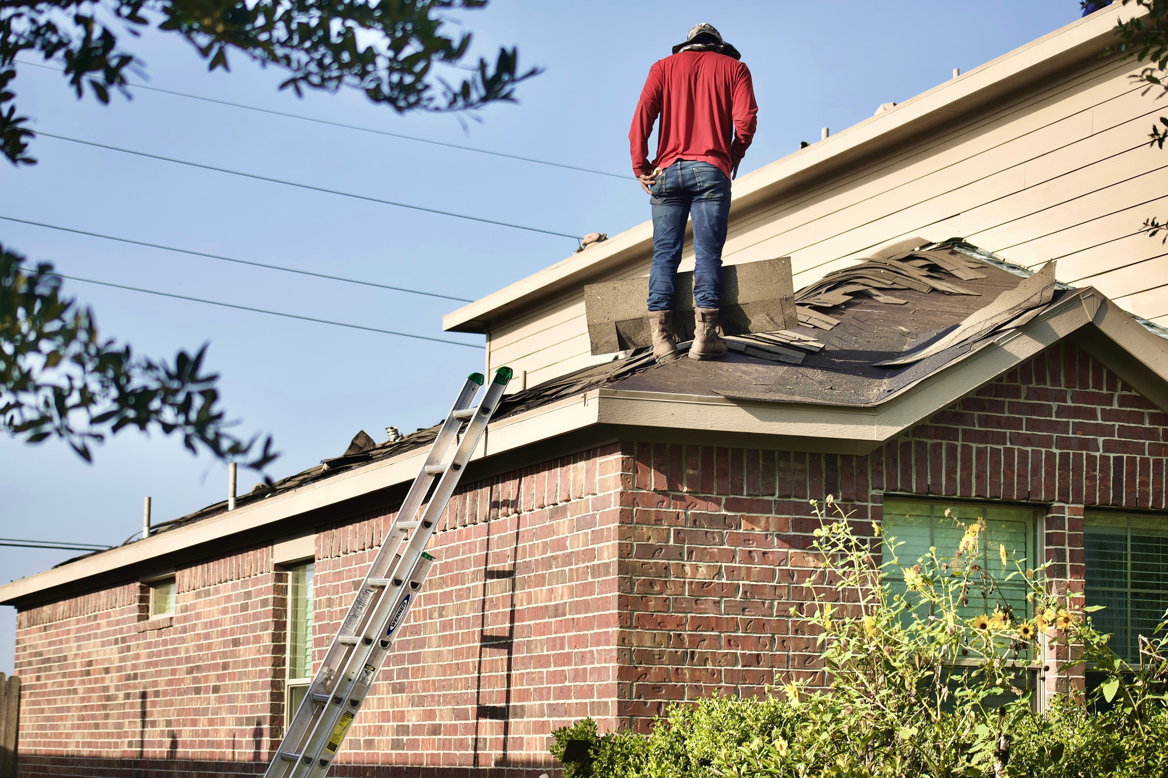 A roofer working on the shingles of a residential roof against a dramatic sky