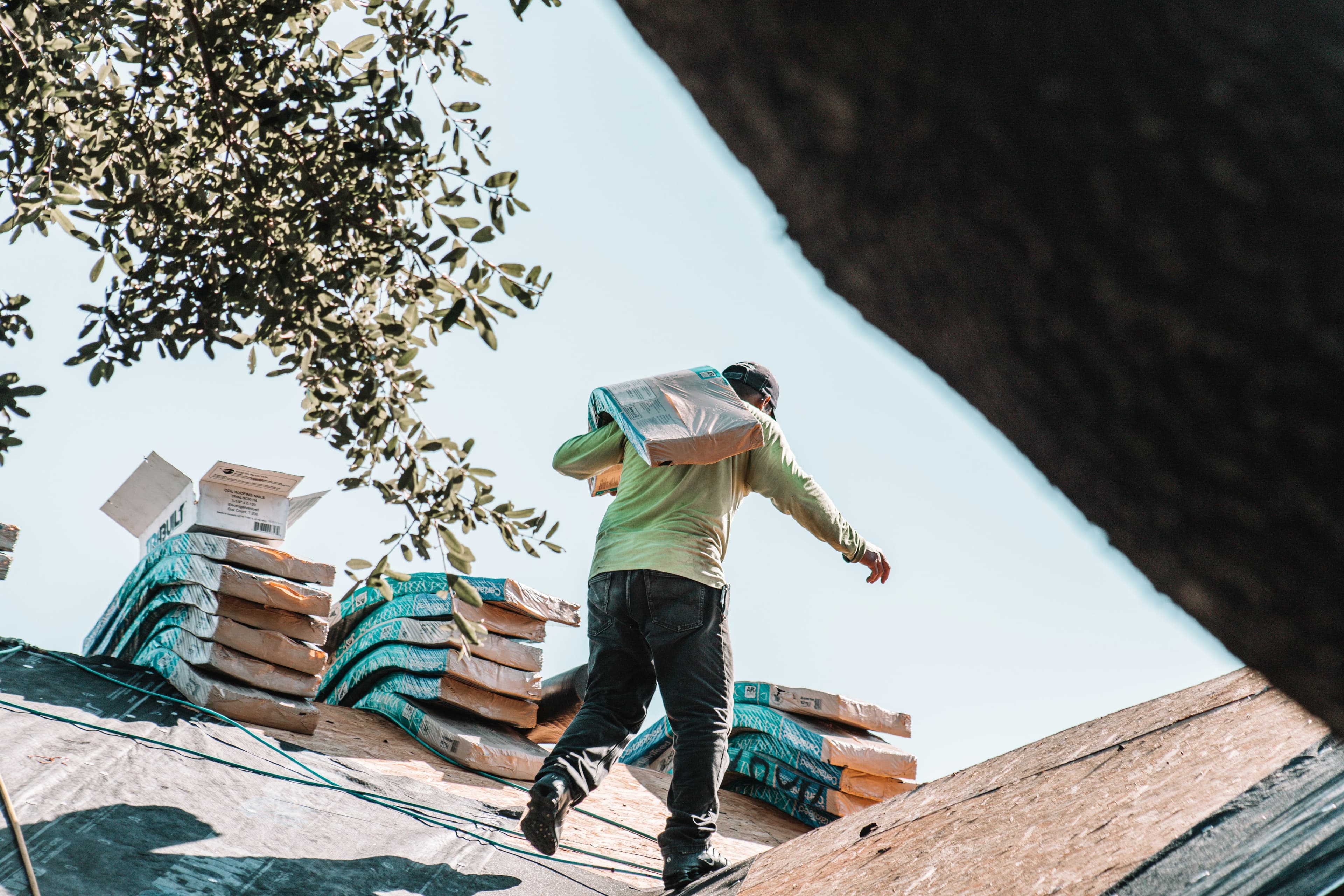 A construction worker carrying roofing shingles up to a roof under installation